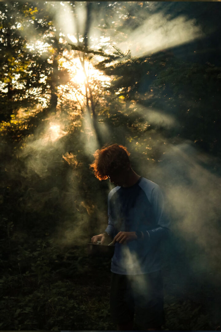 A boy in early morning light surrounded by wood smoke.