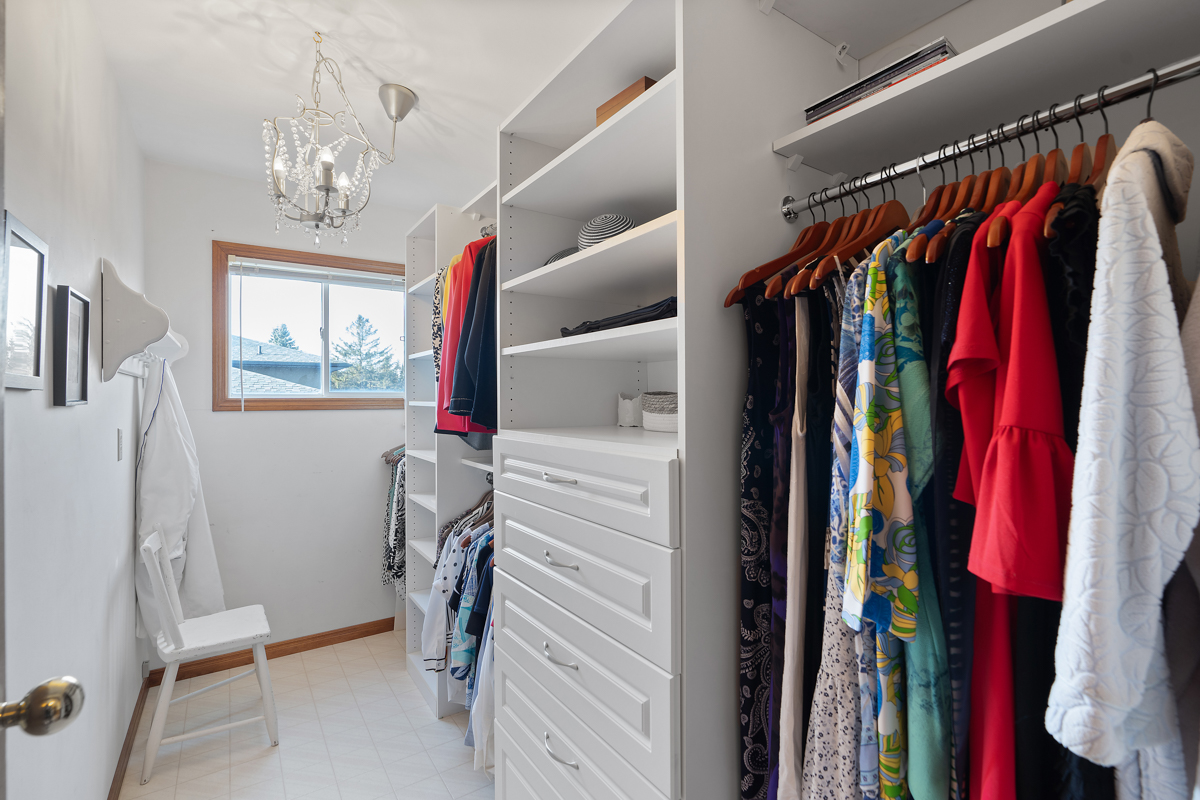 A narrow but bright walk-in closet with two sets of hanging racks and shelves.
