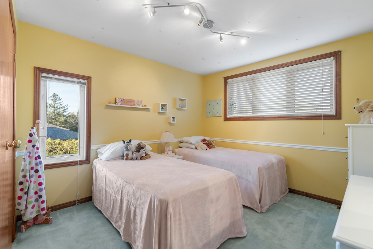 A bedroom with yellow walls, blue carpet flooring, and two twin beds.