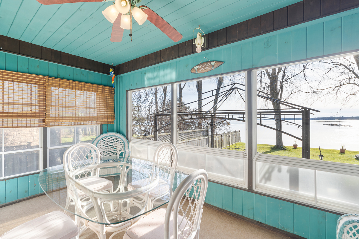 A sunroom with bright turqoise walls, large windows, a ceiling fan, and a clear glass table surrounded by white wicker chairs.
