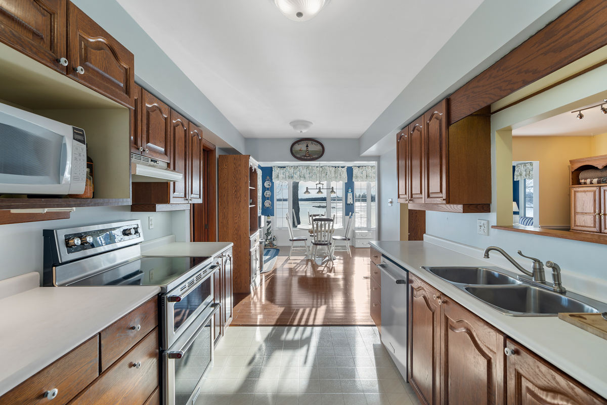 An updated kitchen with brown cupboards and stainless steel appliances. The kitchen flows into a bright dining area.
