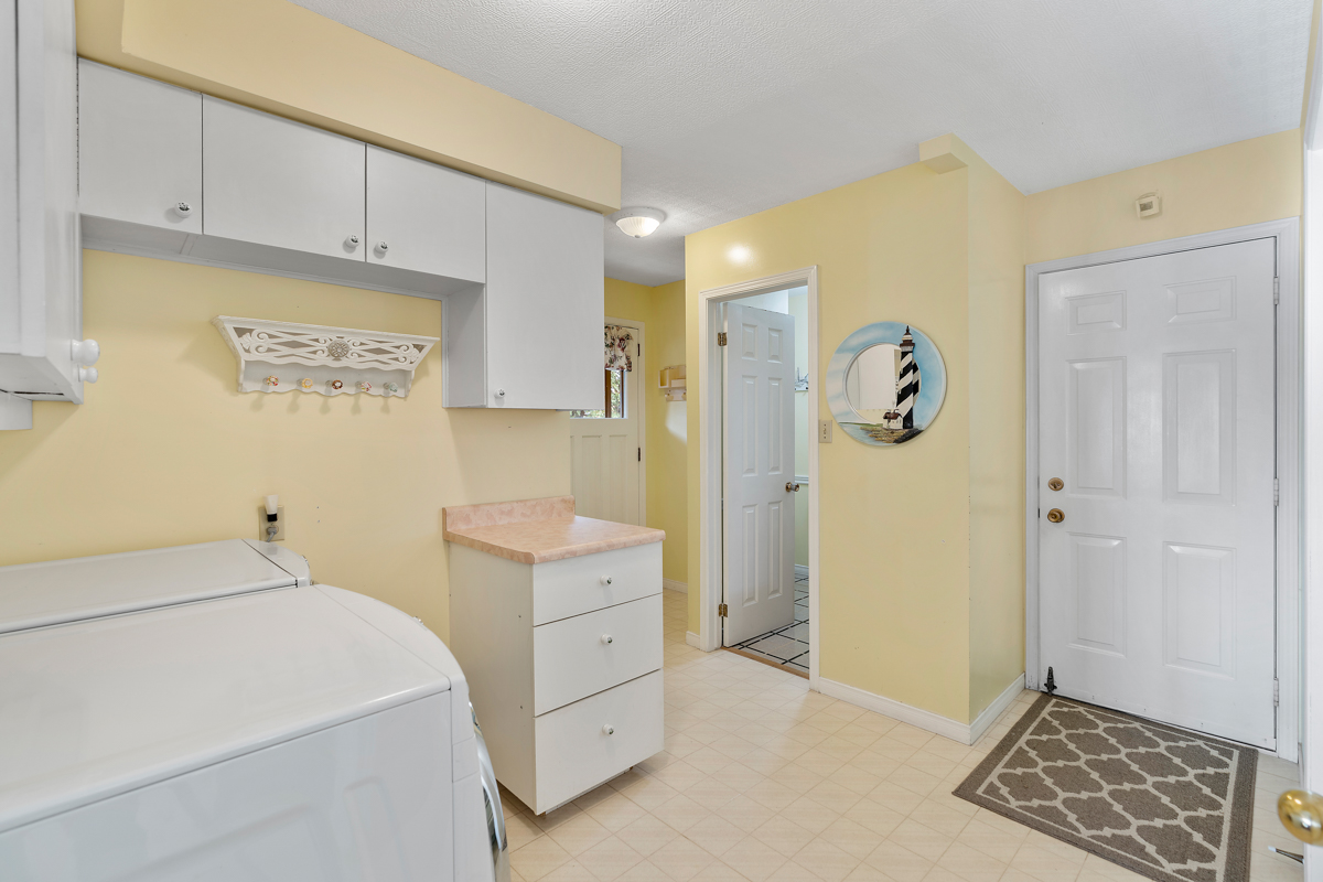 A spacious laundry room with a washing machine, a dryer, white cupboards, and yellow walls.