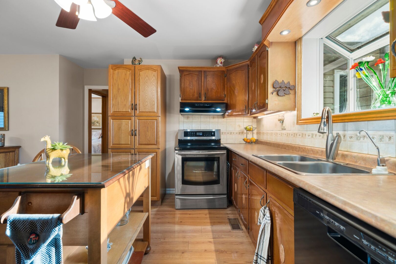 A kitchen with wooden cupboards, hardwood flooring, a stainless steel oven, and a small island.