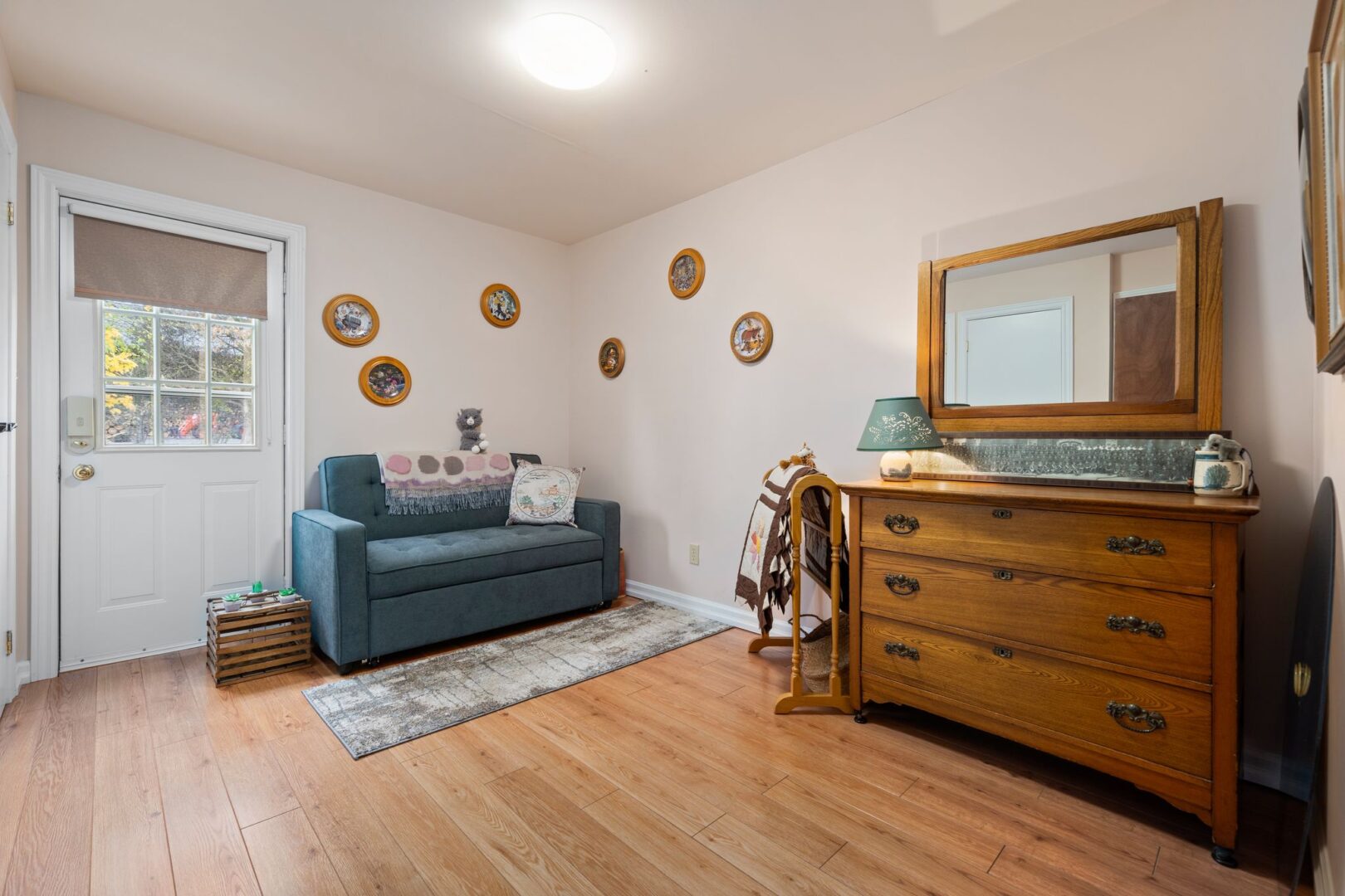 A bright sitting room with hardwood floors, a couch, and an exterior door leading to outside.