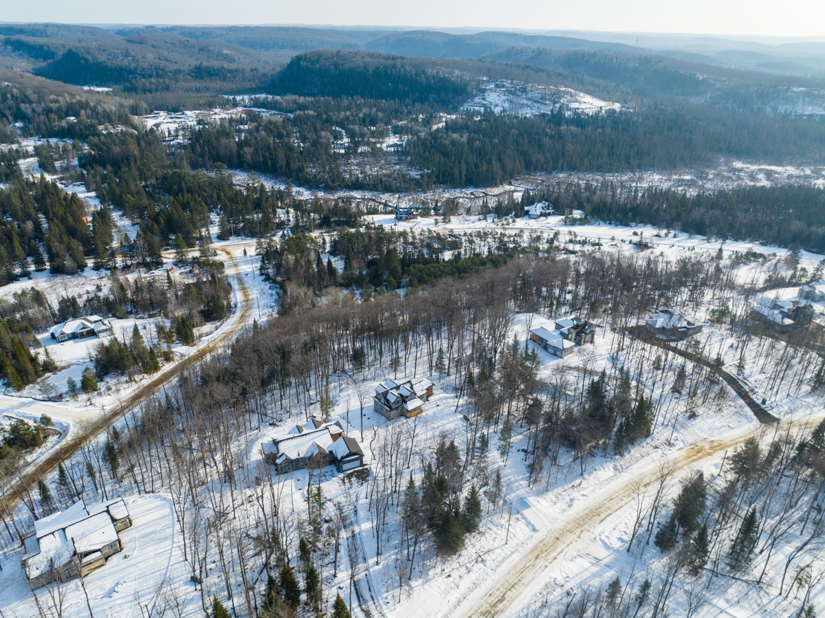 Overhead view of a rural area in winter. There is snow on the ground and the trees are bare. A few houses are scattered along narrow roads.