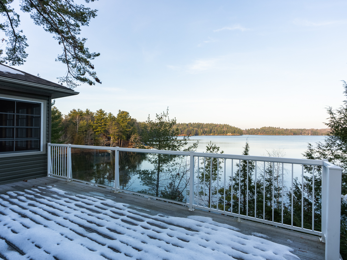 A wide snow-covered deck with a white railing looks out over a lake.