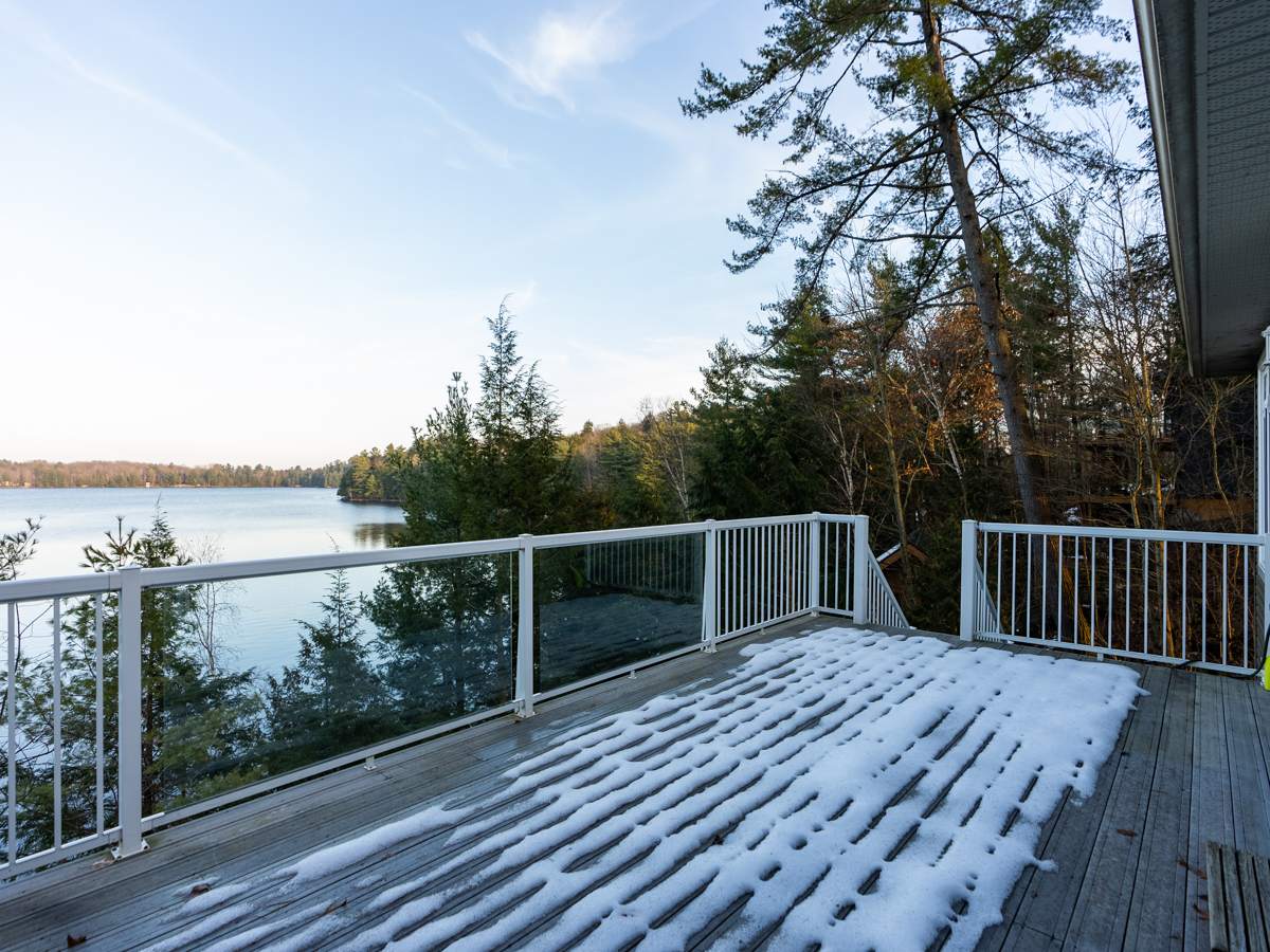 A wide snow-covered deck with a white railing looks out over a lake.