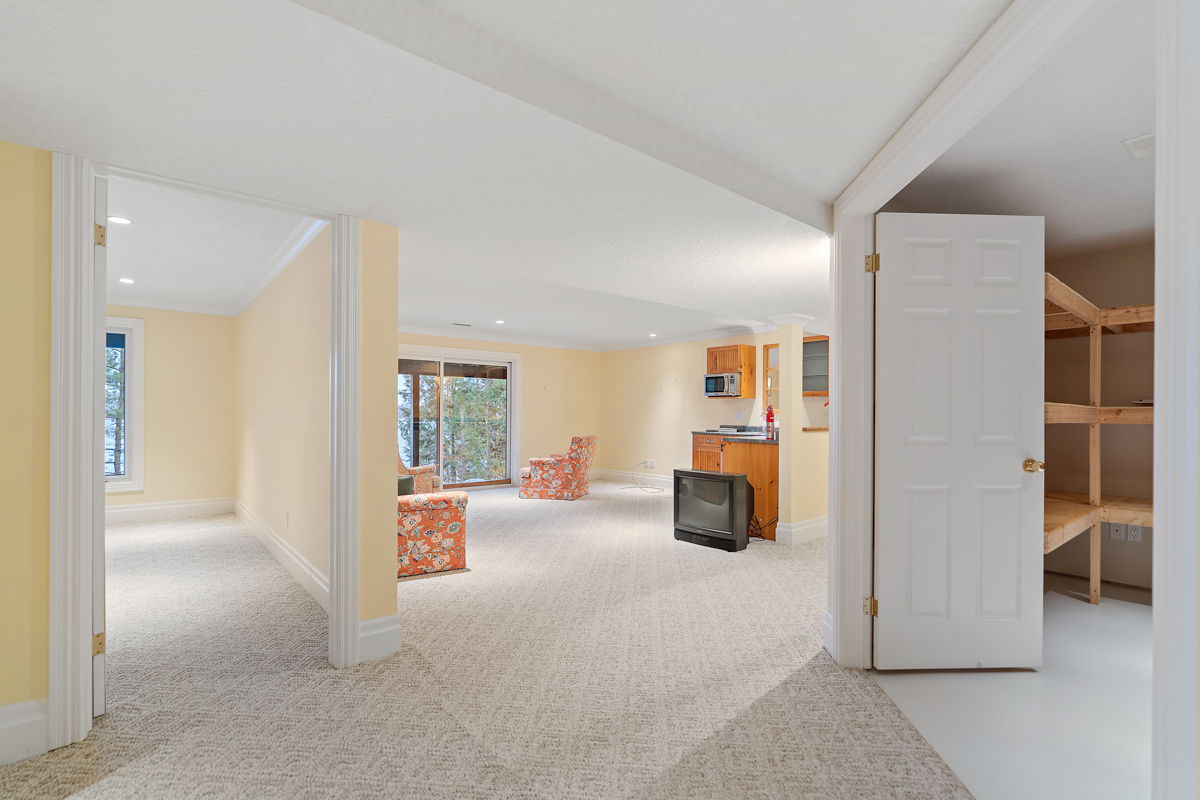 A bright walk-out basement with yellow walls and carpet flooring. A doorway to the right leads into a large storage room.