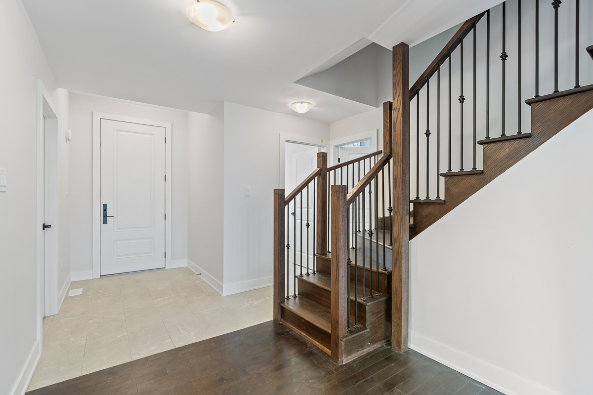 In a small foyer area, cream-coloured tile meets dark hardwood flooring in the middle. A dark wood staircase the same colour as the wood floor leads upstairs.