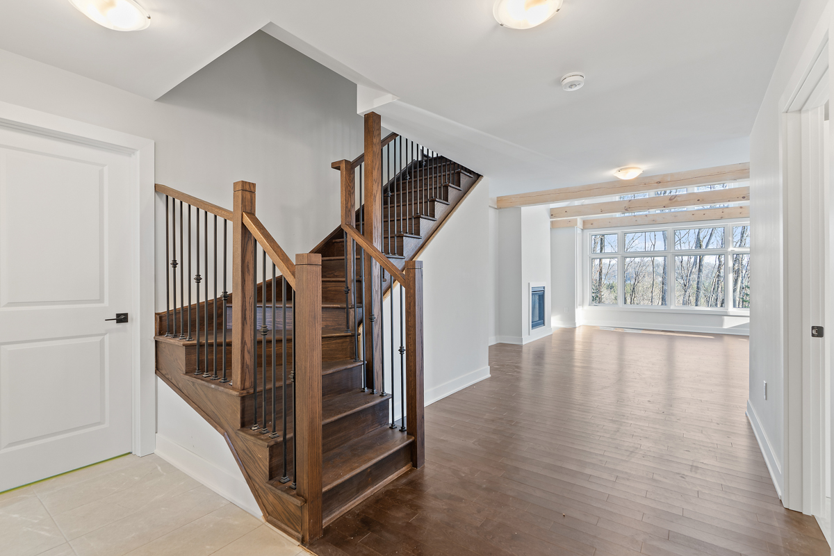 A house opens up into a bright, open space with dark hardwood floors and lots of natural light. To the left, a dark wood staircase leads upstairs.