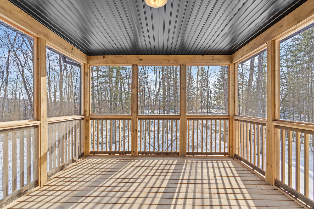 A bright, empty sunroom with wood framing and a black panelled ceiling.