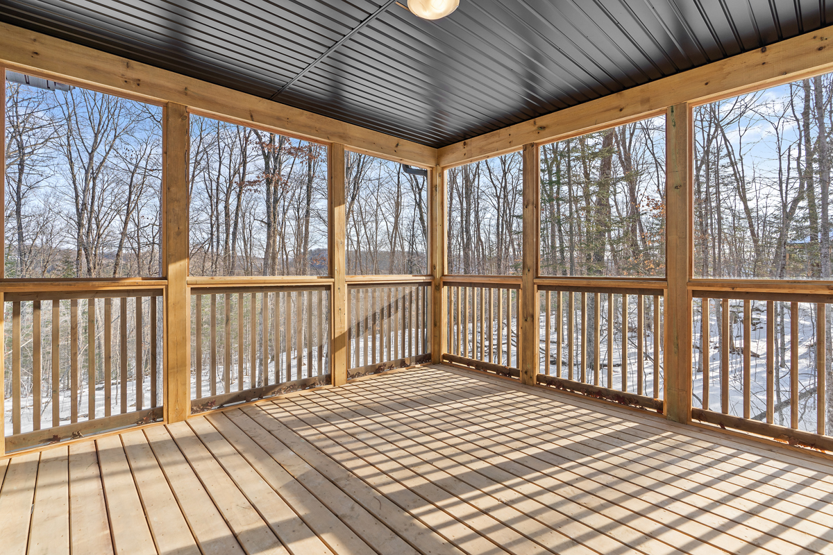 A bright, empty sunroom with wood framing and a black panelled ceiling.