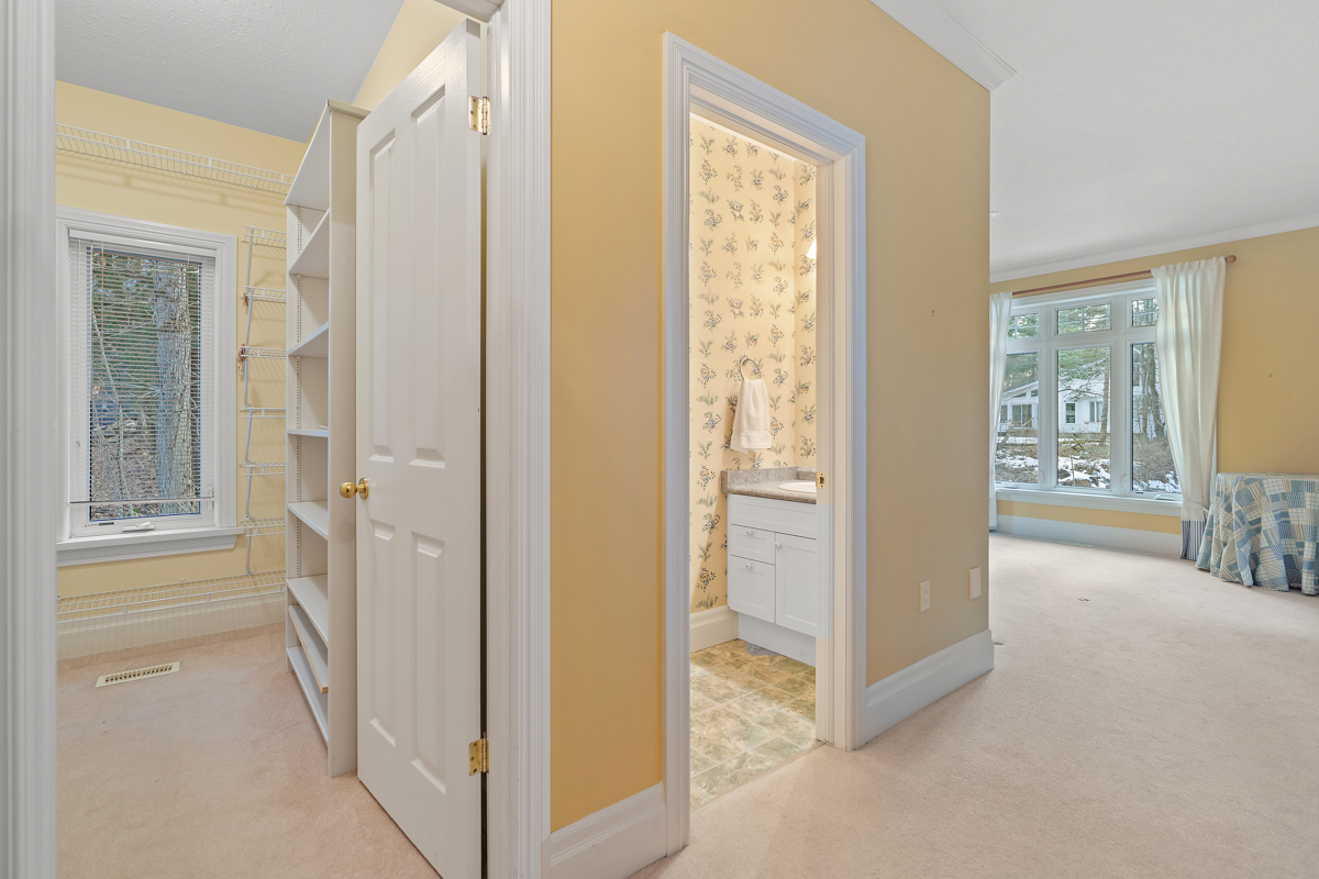 The entrance to a primary bedroom. Two doorways lead into a bathroom and a closet. The walls are yellow and the room has carpet flooring.