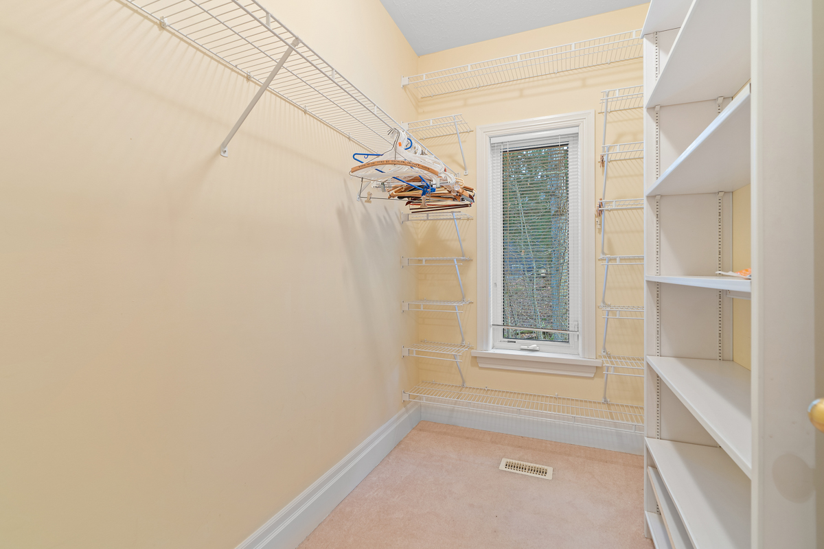 A narrow walk-in closet with one wall of shelves and one with hanging racks.
