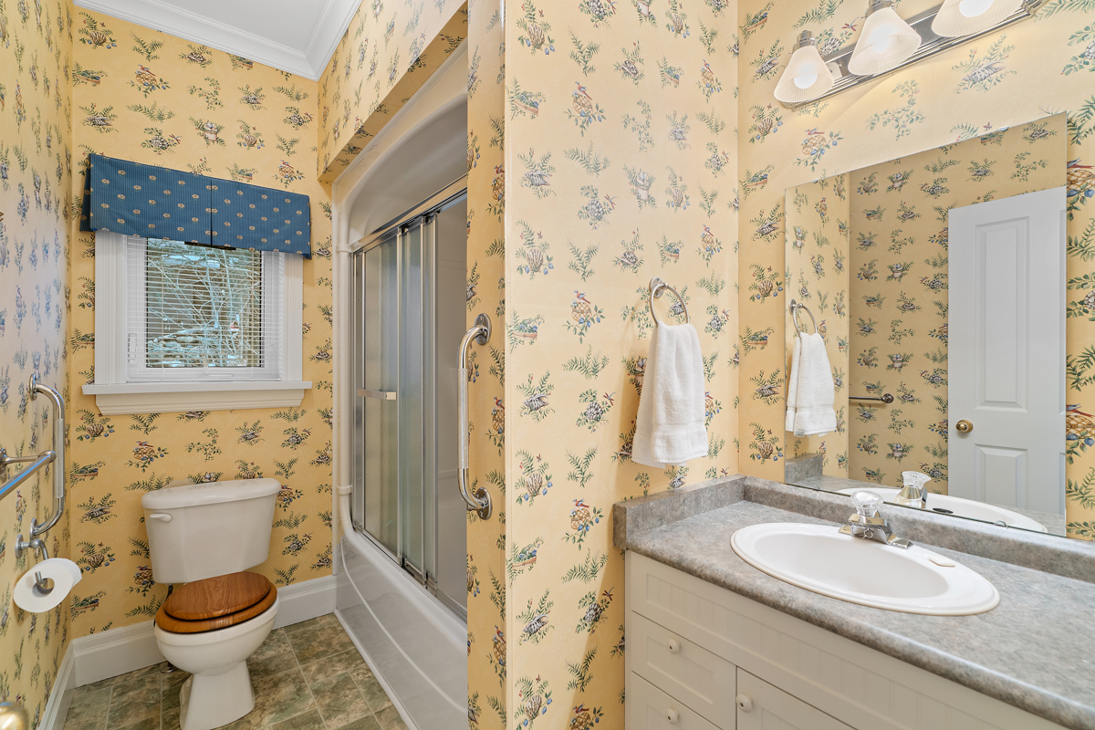 An ensuite bathroom with yellow floral-print wallpaper, a toilet, a sink, and a walk-in shower.
