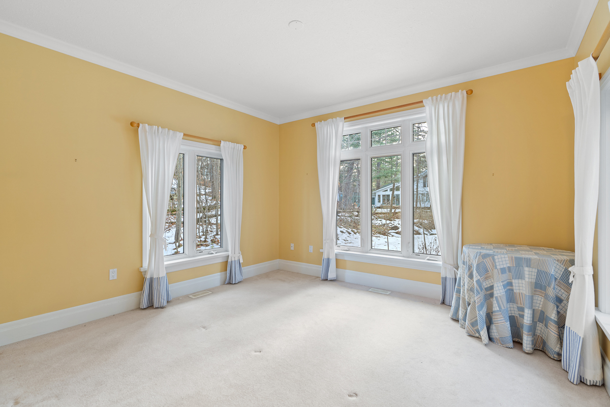 A bright, empty bedroom with yellow walls, big windows, and carpet flooring.