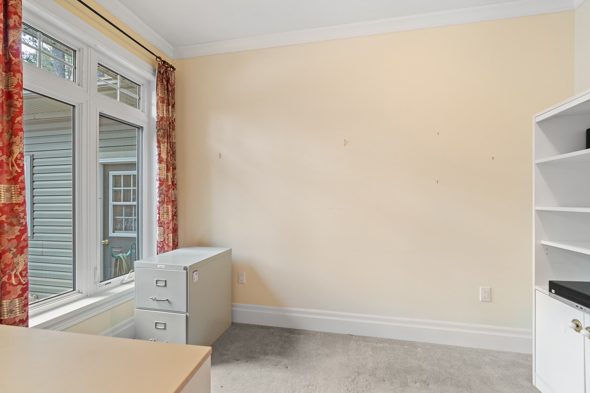 A small but bright room with a big window, light yellow walls, and carpet flooring. A small filing cabinet sits by the window.