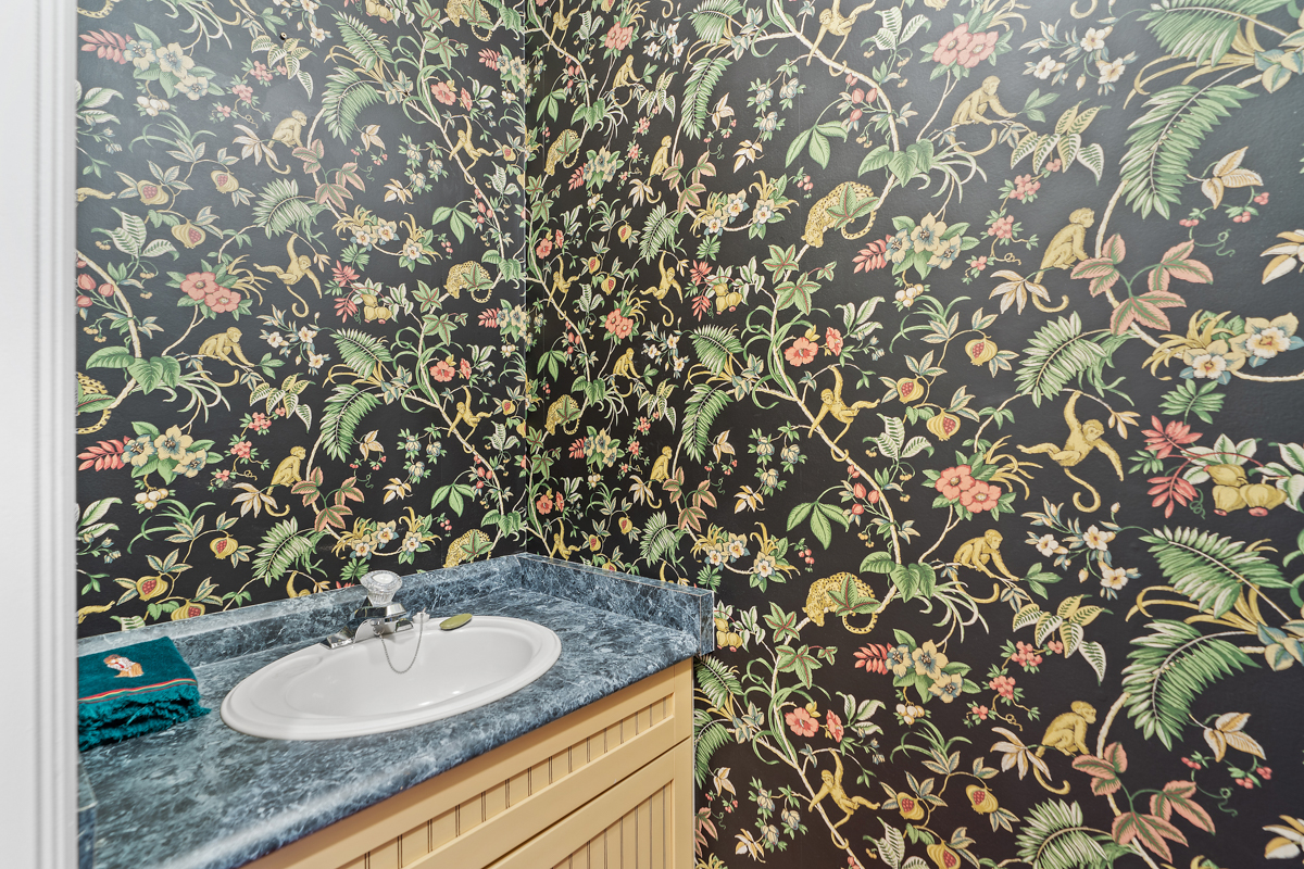 A small bathroom with a sink and dark printed wallpaper with flowers, vines, and monkeys.