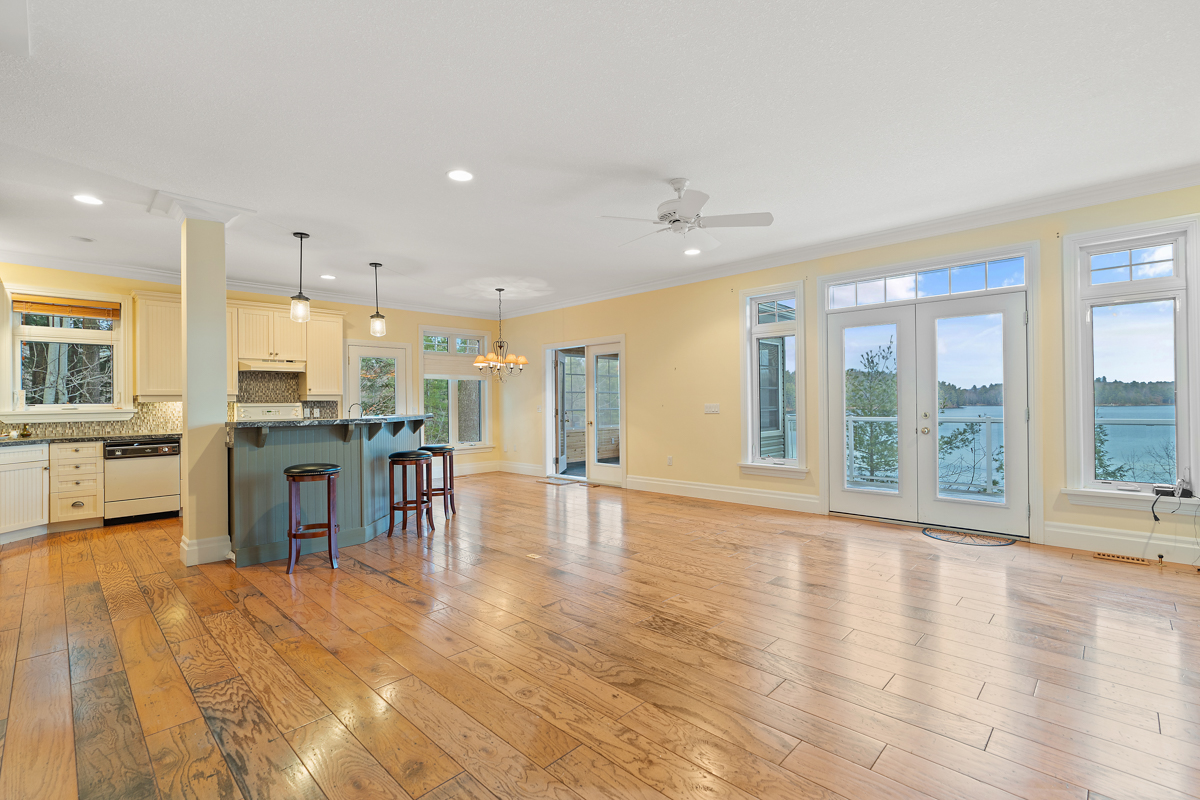 A large, open-concept, empty space with hardwood floors and big windows. There is a kitchen island off to the left. Double doors lead out to a deck.