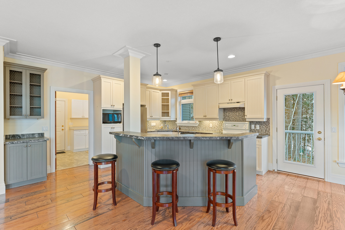A curved kitchen island with barstool seating, in a bright kitchen with hardwood floors.