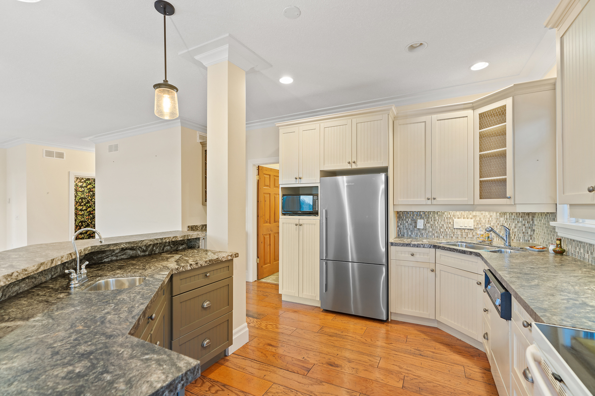 A big, bright kitchen area with lots of countertop space, hardwood floors, and cream-coloured cabinets. The appliances are mostly older, and there is a stainless steel fridge set into the cabinets..