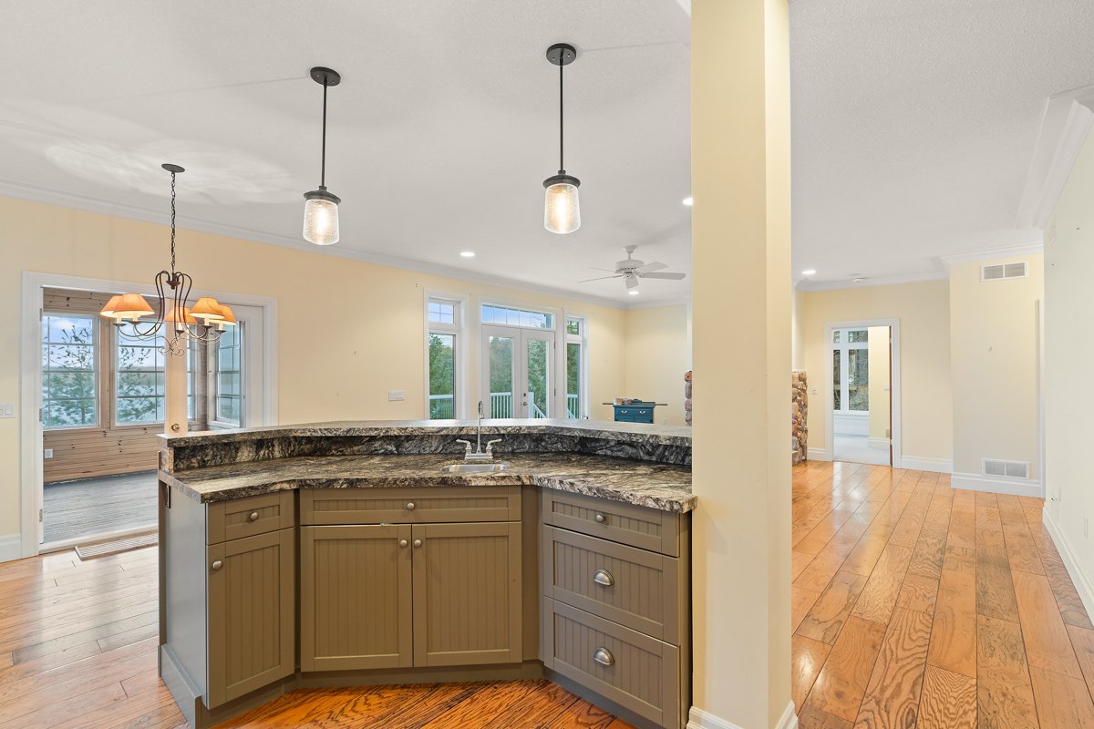 A curving kitchen island with a sink and olive-coloured cabinets. A couple lights hang down about the island.