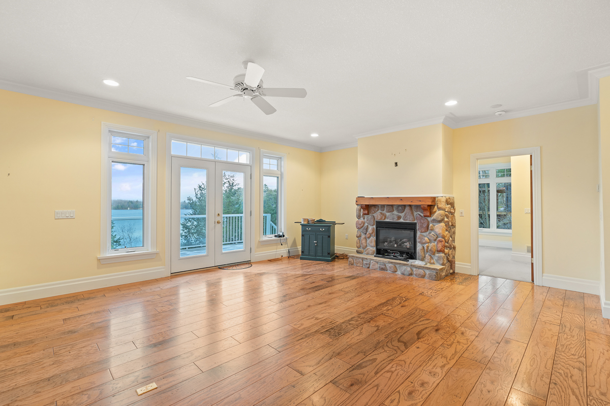 A bright, empty living area with hardwood floors, a fireplace, and double doors that lead out to a deck.