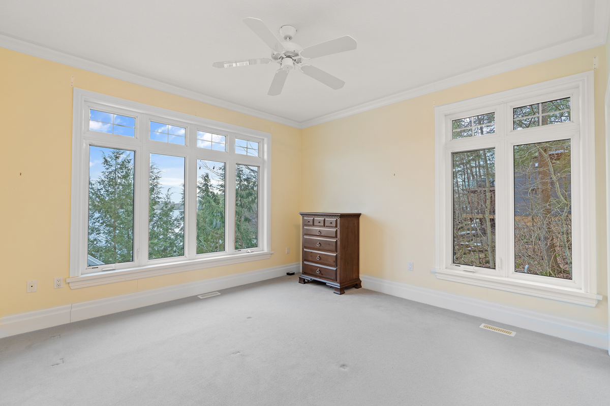 A bright, empty room with big windows, light yellow walls, and carpet flooring.