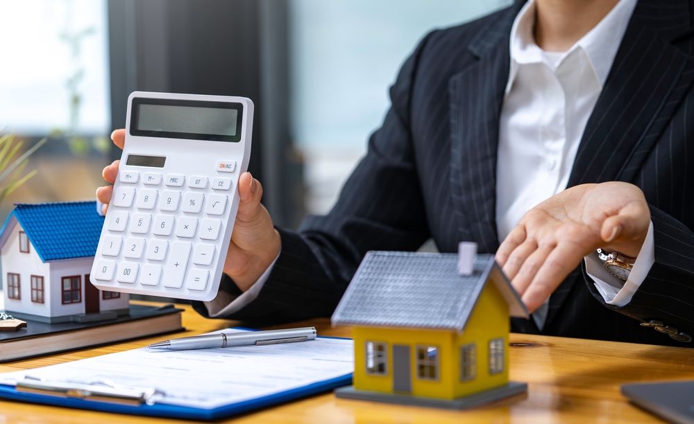 woman holding a calculator beside a miniature house to indicate the appraisal value