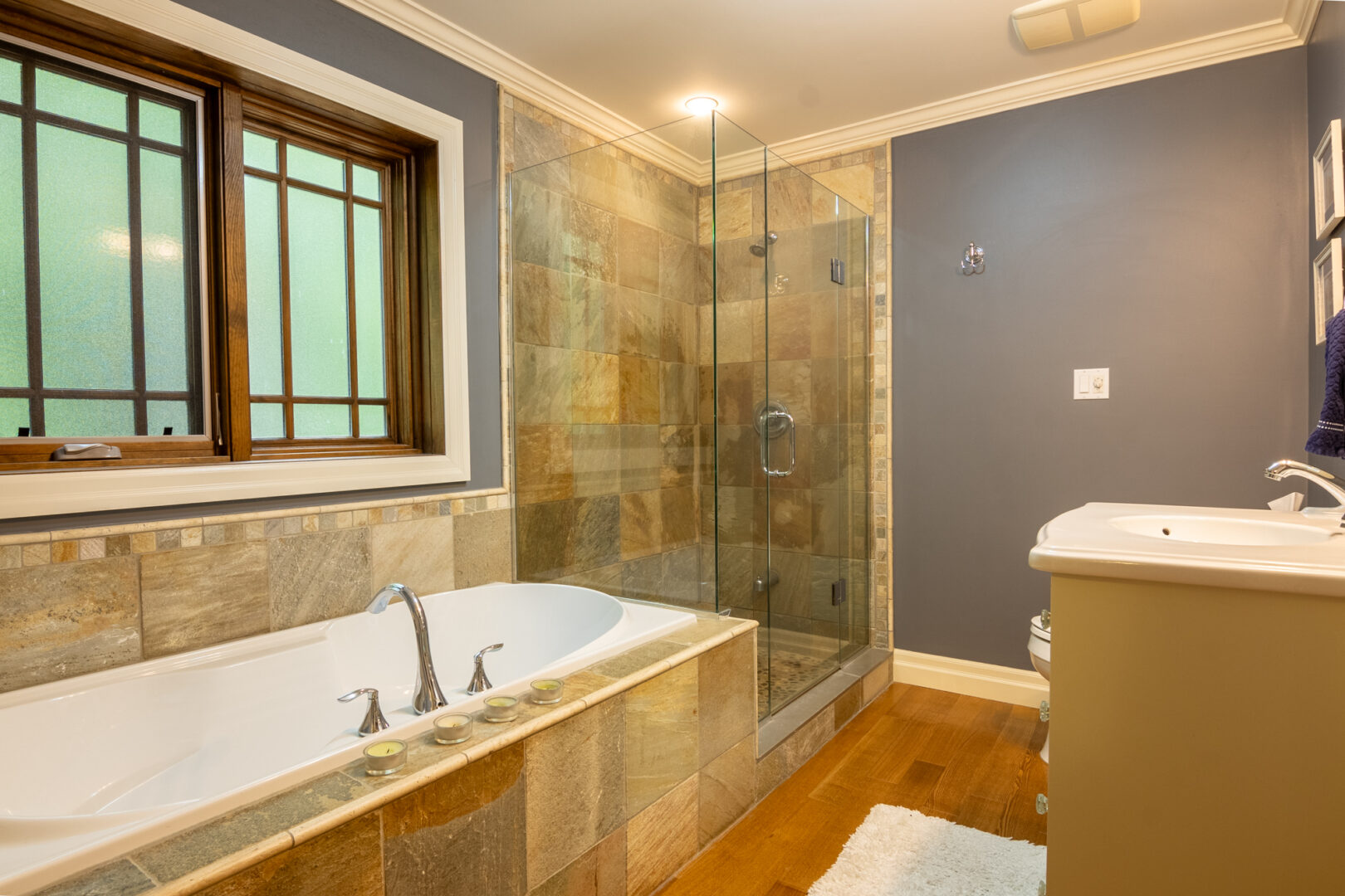 A big bathroom with hardwood flooring, a bathtub, a walk-in shower, a toilet, and a sink.
