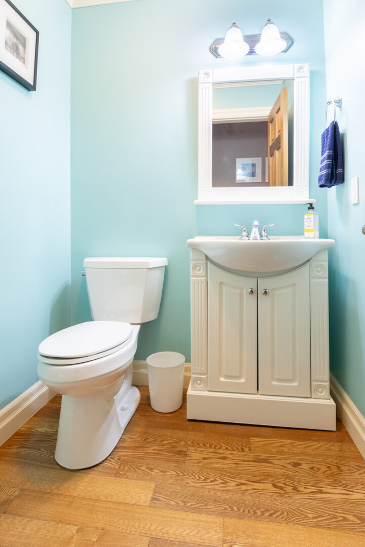 A small bathroom with bright blue walls, hardwood flooring, a toilet, and a sink.