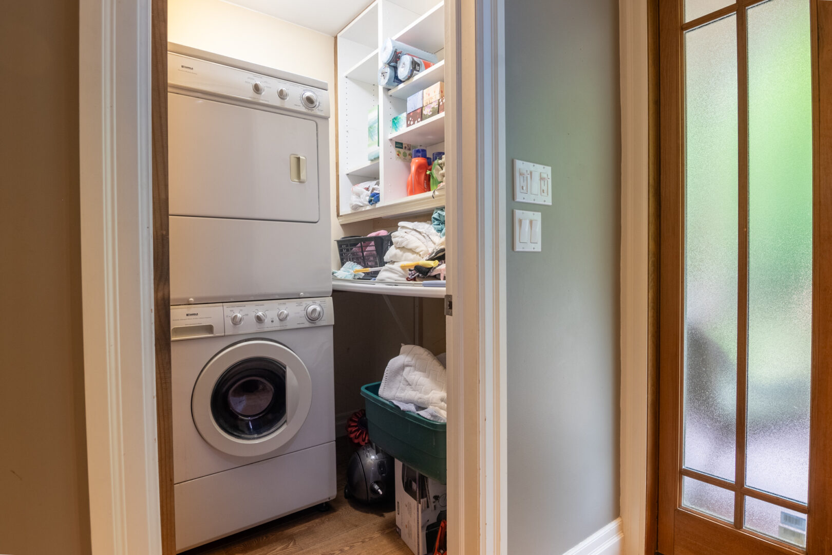 A closet space with shelves and a stacked washing machine and dryer.