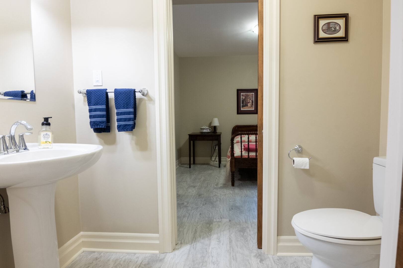 A small bathroom with a toilet and a sink. A doorway leads from the bathroom to a bedroom.