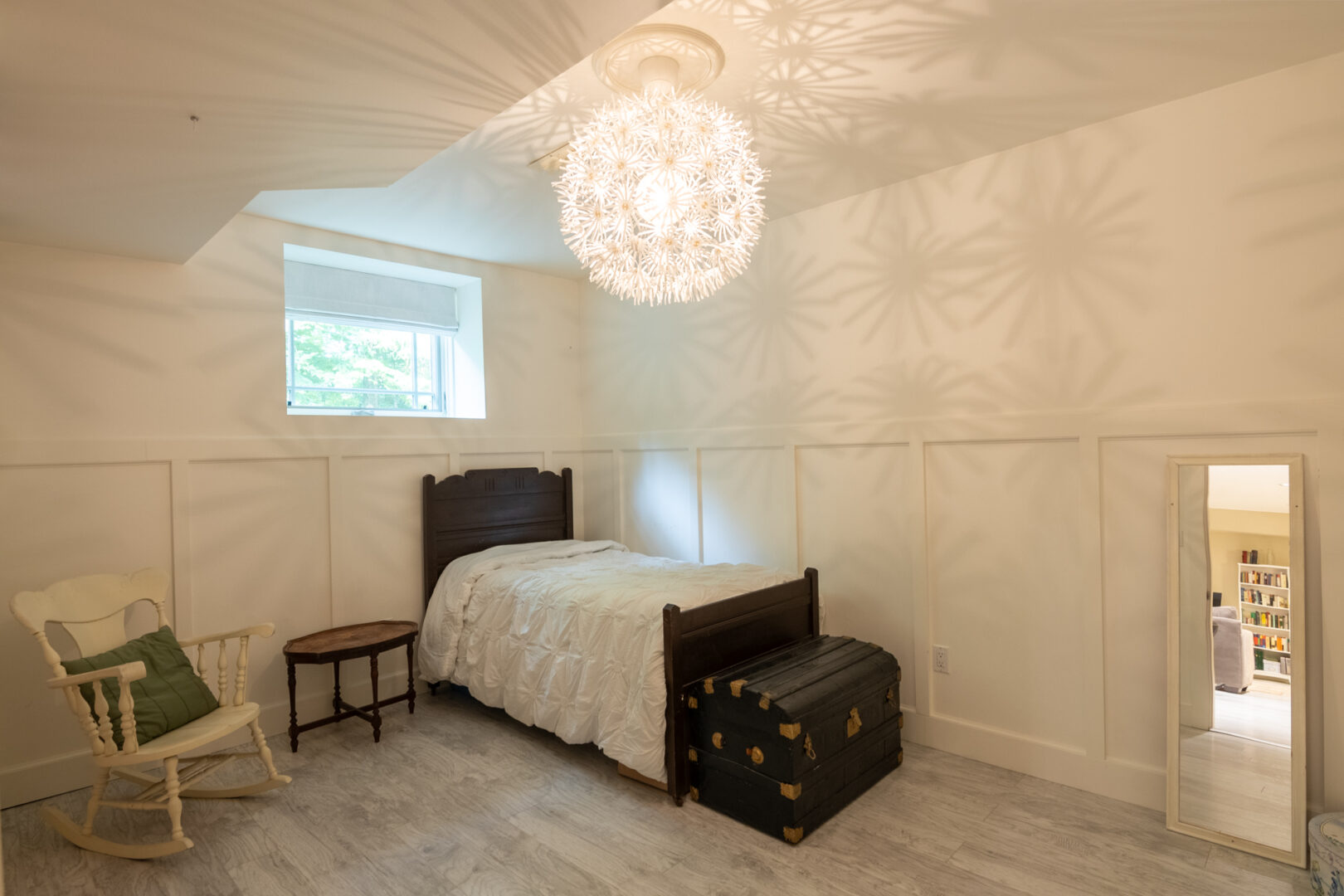 A room with a small window, a small bed, and a round light fixture surrounded by flowers.