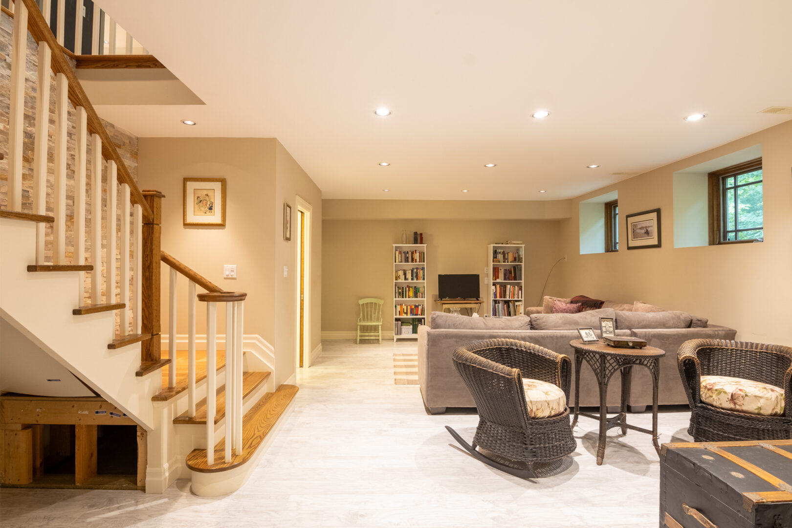 A lower-level living area at the bottom of a staircase, with a couple couches, bookshelves, and a television.