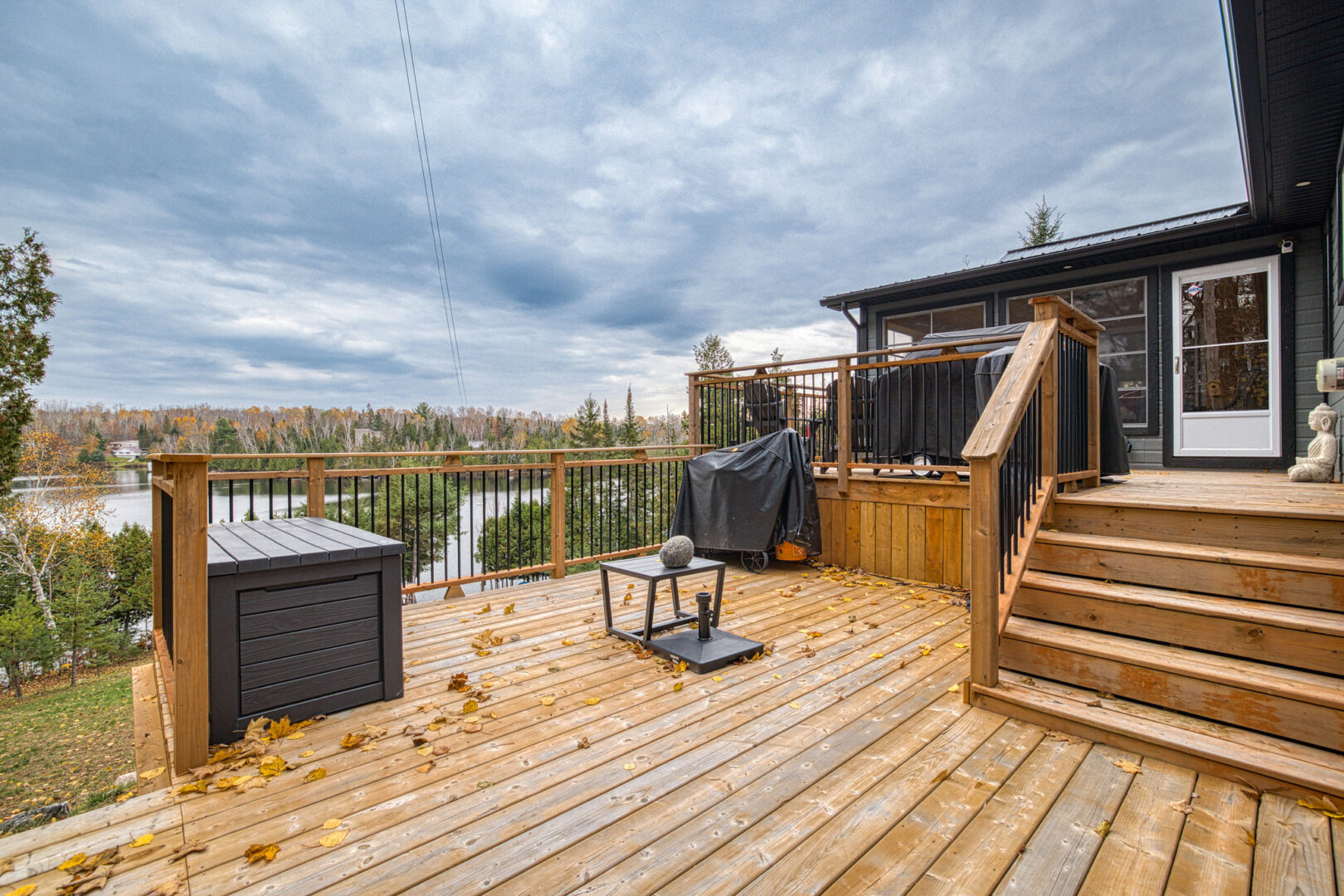 A large wooden deck with two levels extends off the back of a waterfront bungalow.