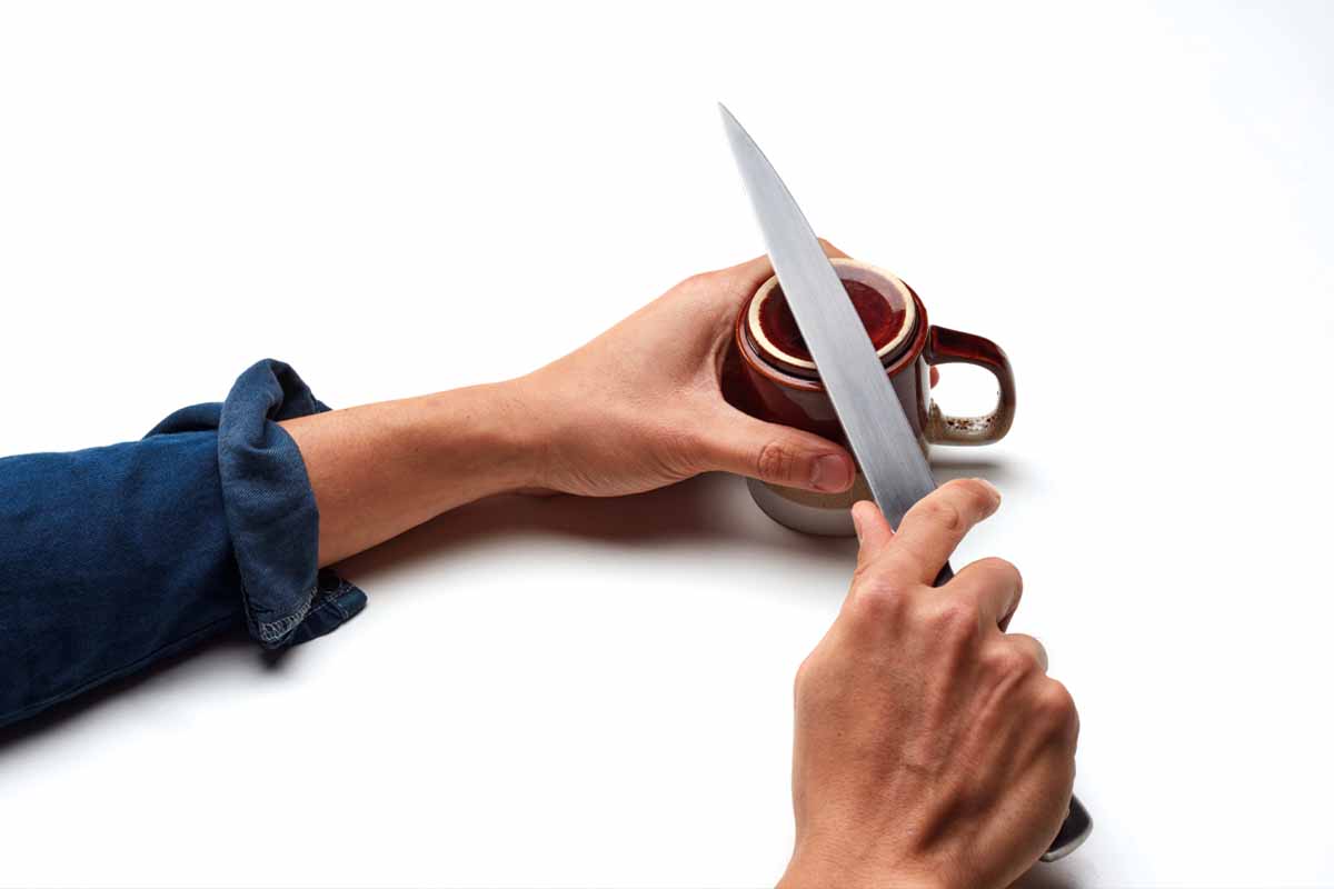 Hands sharpening a knife on the bottom of a mug