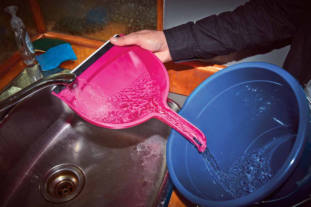 Someone filling a water bucket using a dustpan