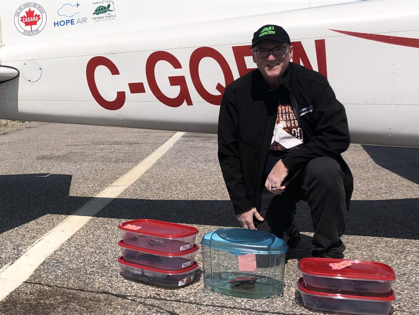 a man kneels in front of a plane with containers of turtles to be taxied in front of him