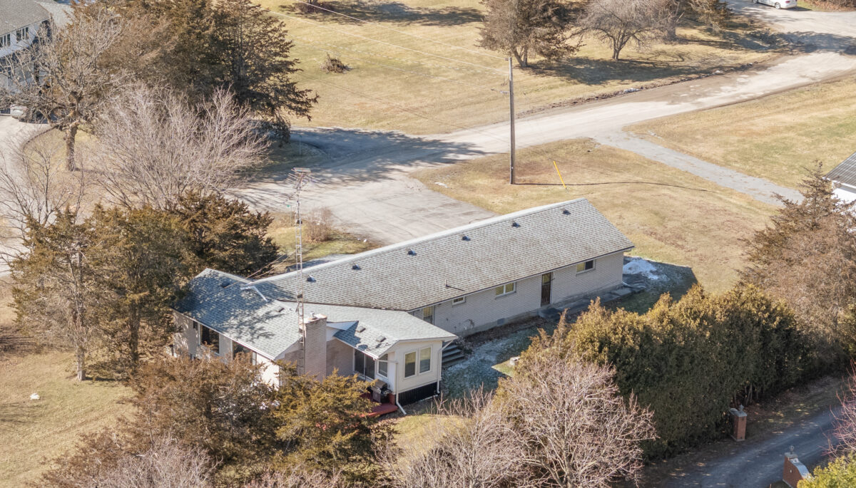 Overhead view of a bungalow sitting on a grassy area, surrounded by some trees.