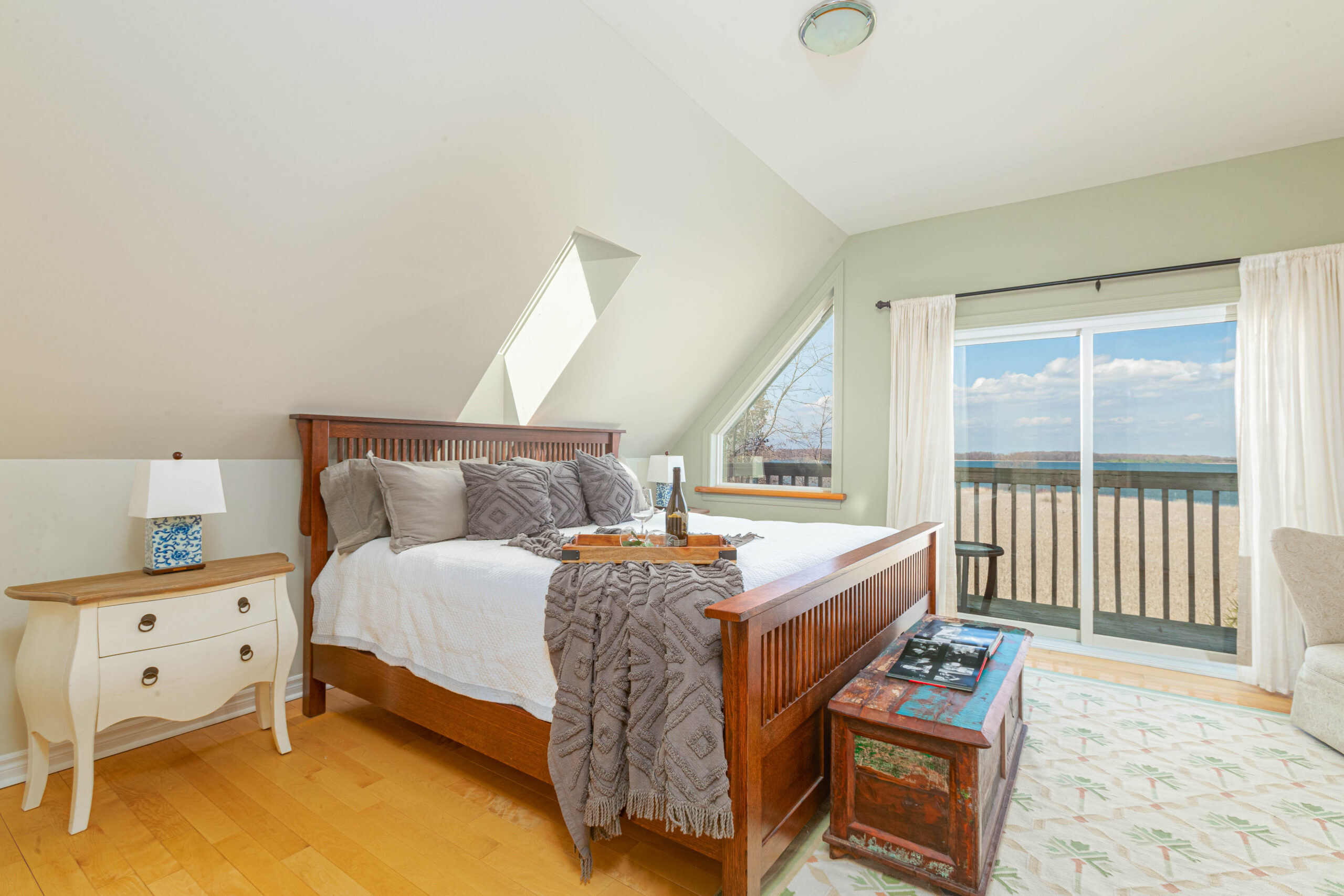 A big bedroom with a sloping roof and a narrow skylight window over a big bed. Sliding glass doors open out to an exterior balcony.