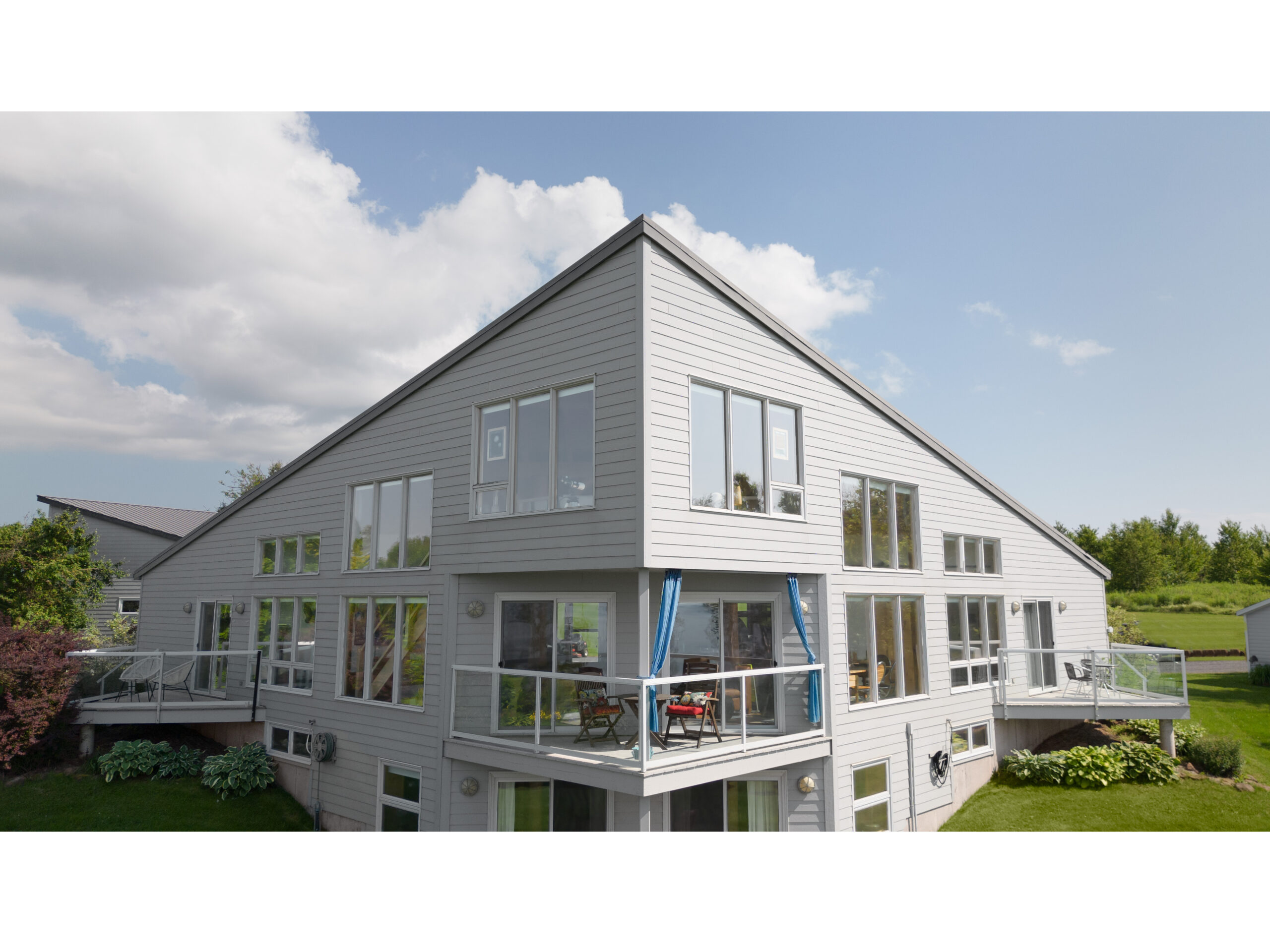 A big home with a unique design. A walls come together on an angle to a point, like the bow of a ship. Both sides have lots of windows, in a symmetrical layout, and big decks extend off the home.