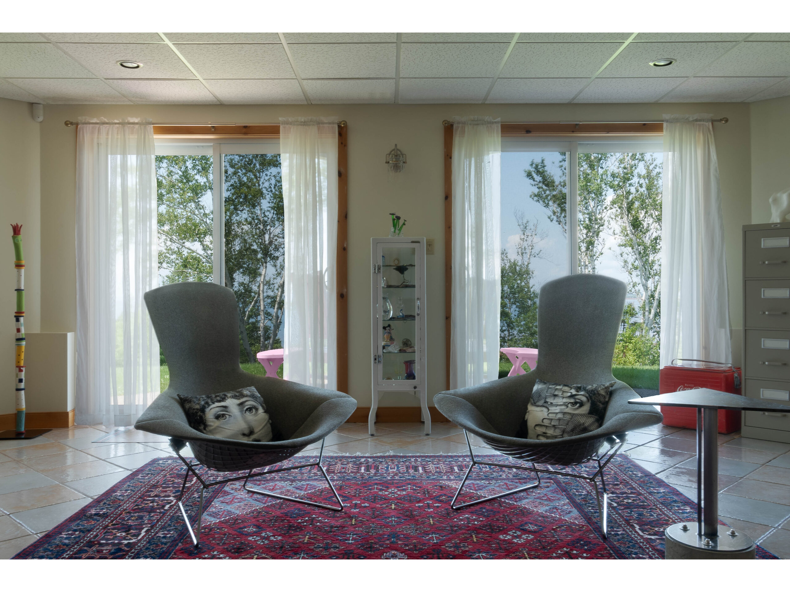 Two chairs sit on a red rug in a bright room.
