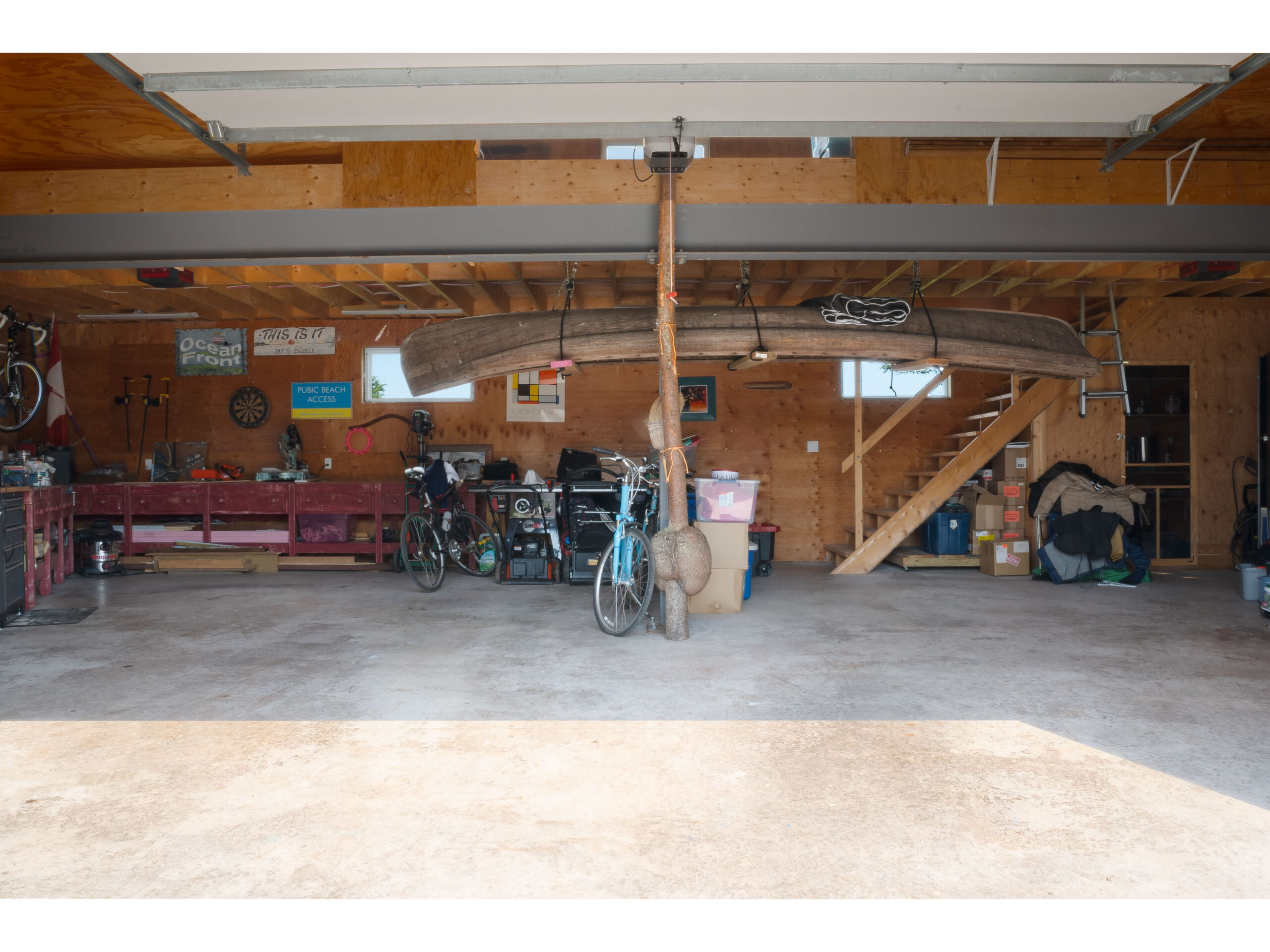 Interior of a big garage space. A canoe hangs from the ceiling, and a long work table lines the walls in one corner.