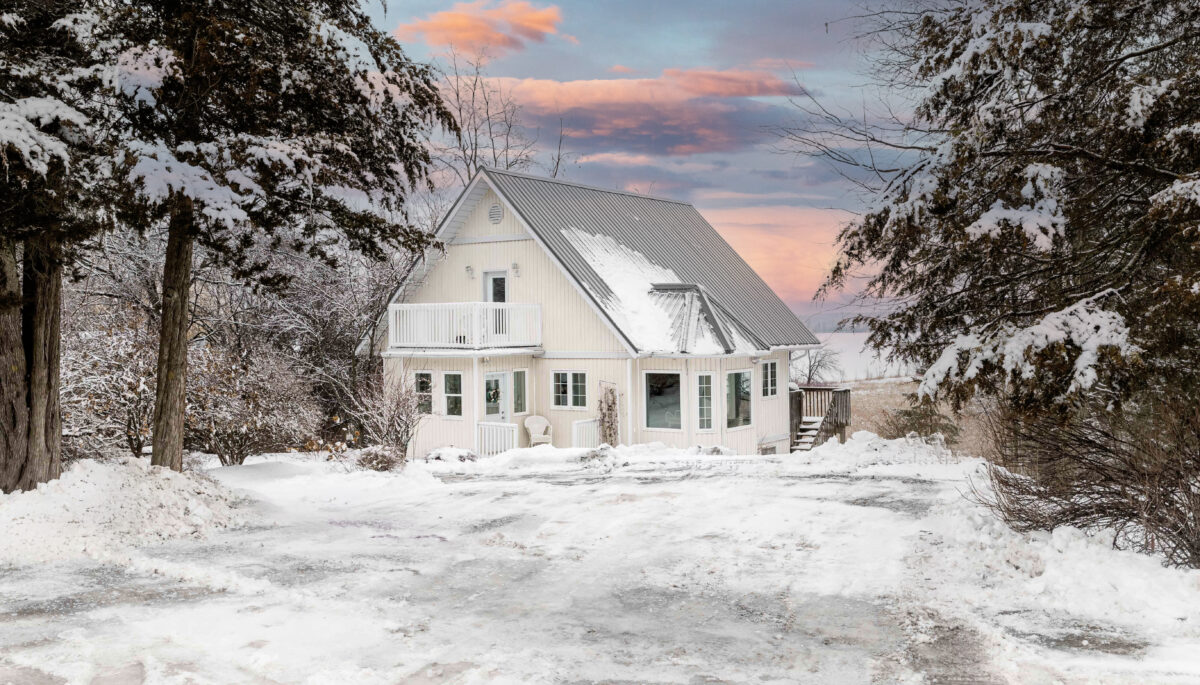 A large home on a snow-covered yard, with large evergreen trees on either side.