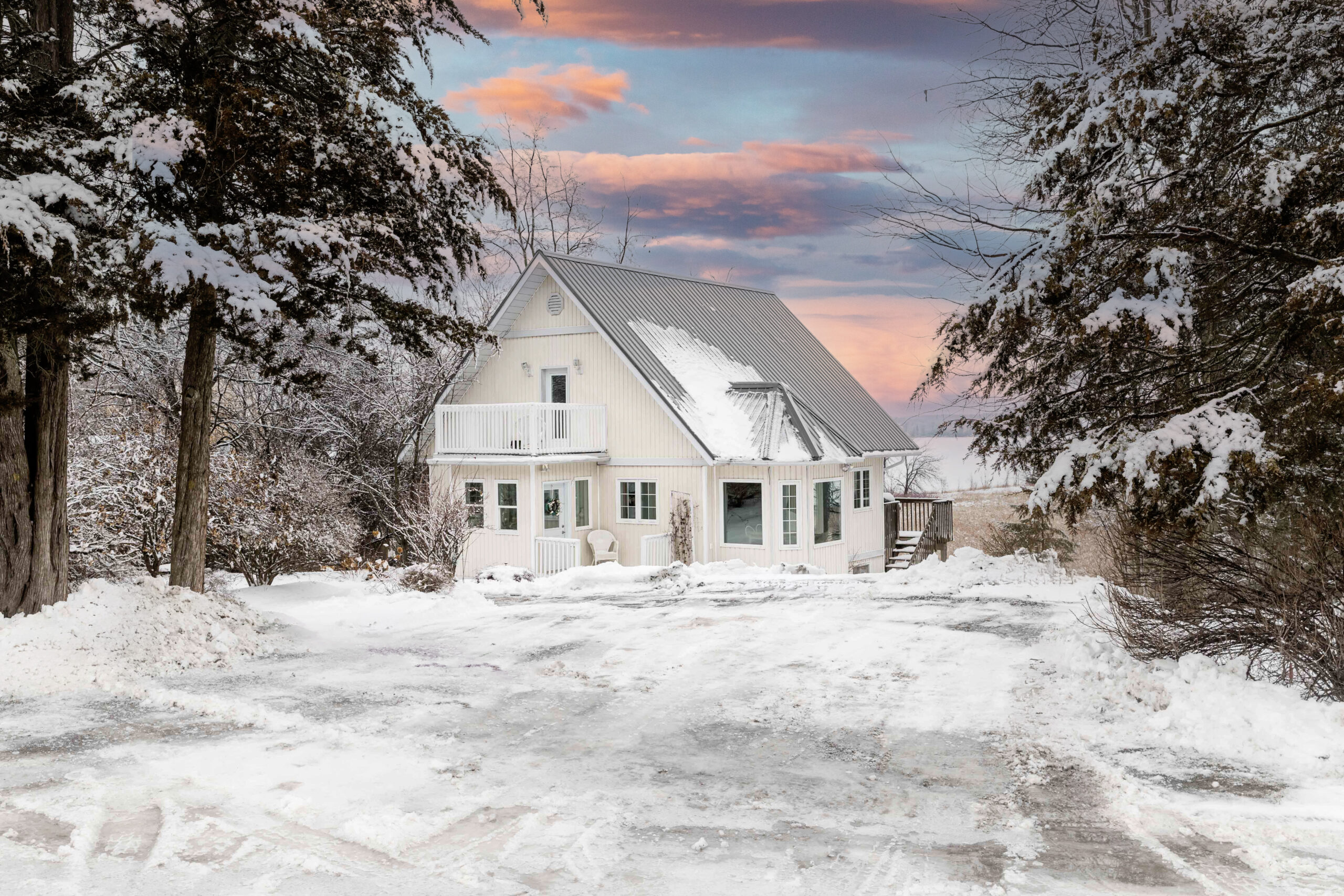 A large home on a snow-covered yard, with large evergreen trees on either side.