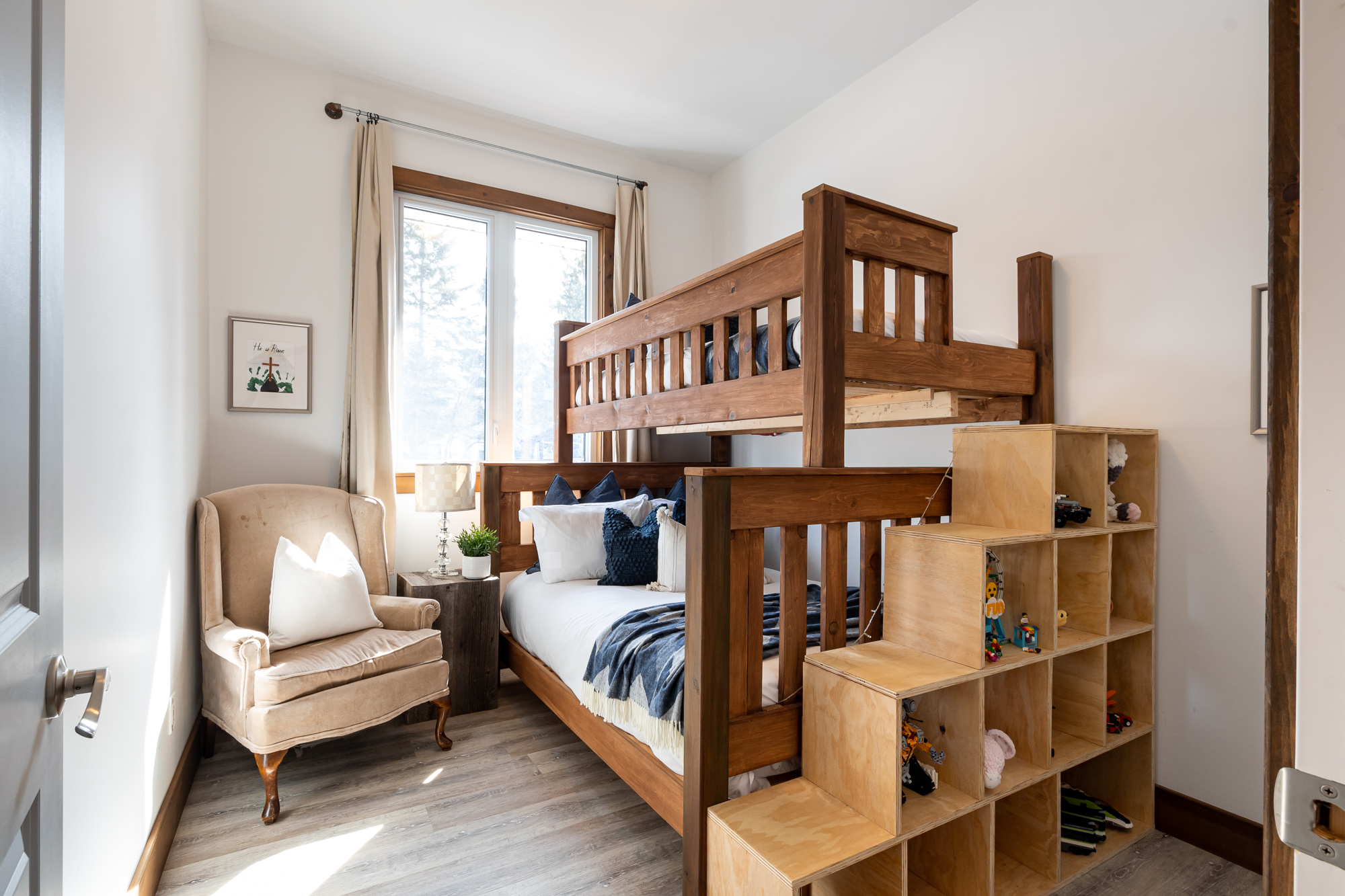 Another guest bedroom with brown-wood bunk beds, stackable storage and a cream chair