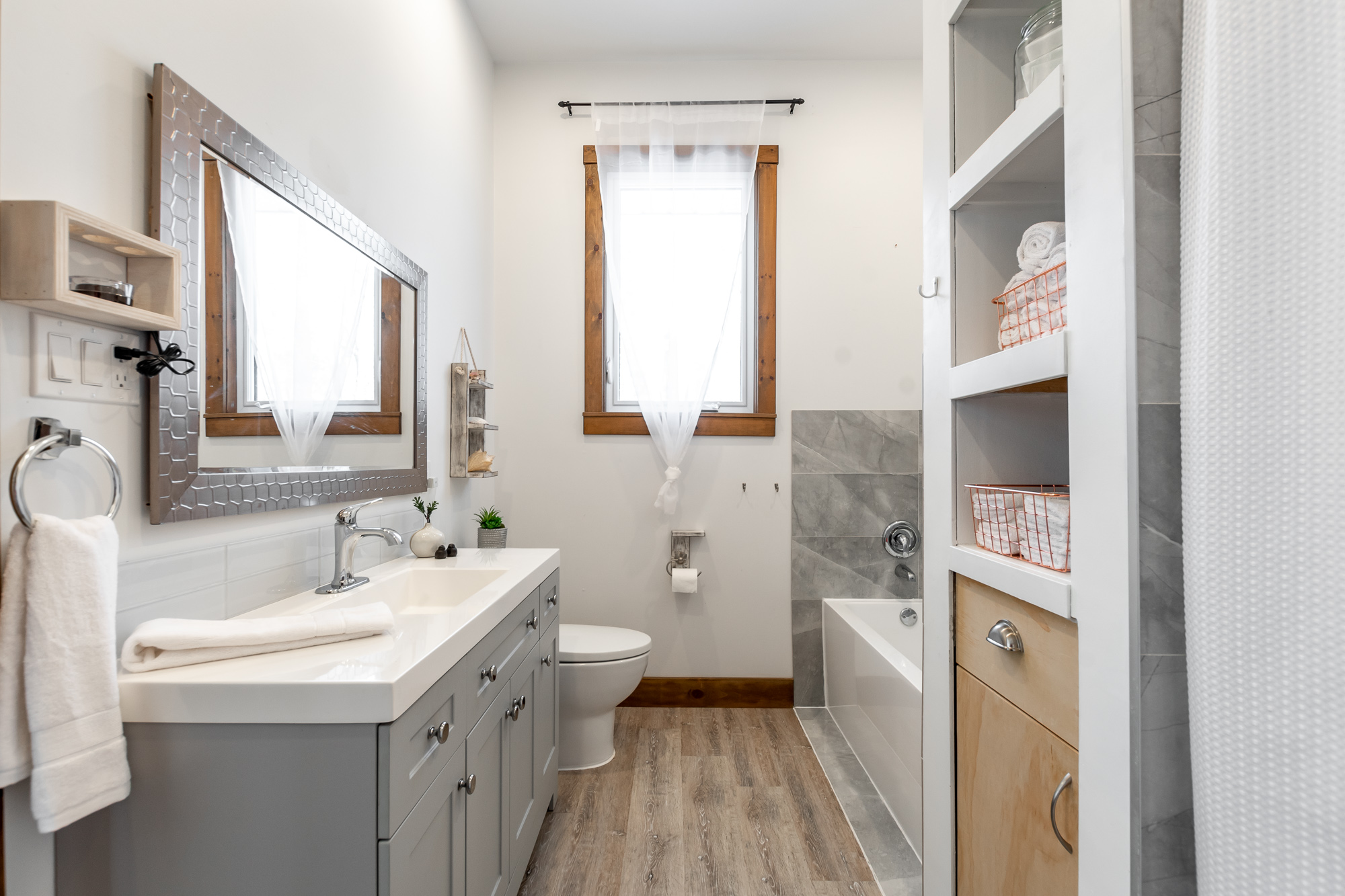 Side view of bathroom with grey vanity and bright mirror that faces a bathtub