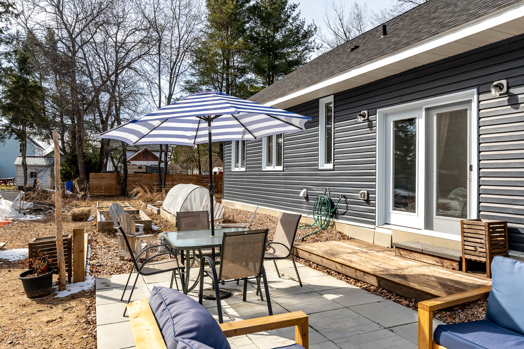 Backyard patio with a dining set, blue and white striped umbrella, and casual seating