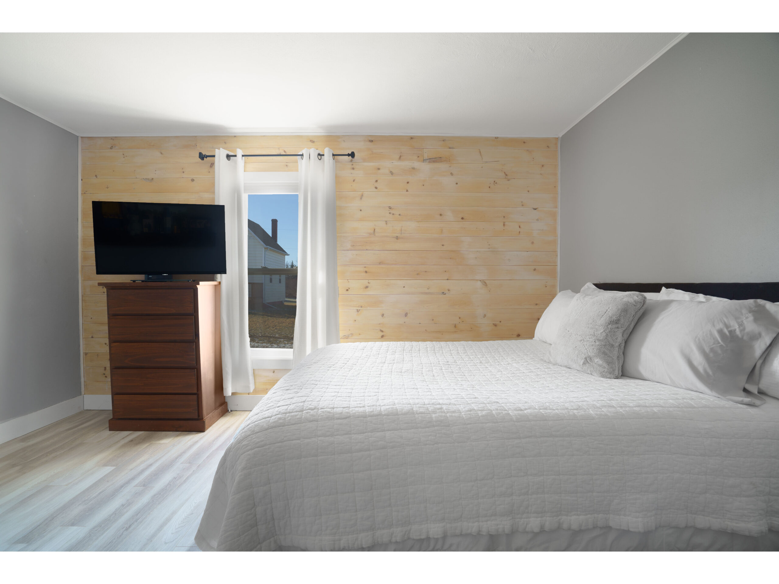 A bedroom with a big bed, a wood-panelled wall with a window, and a television on top of a dresser.